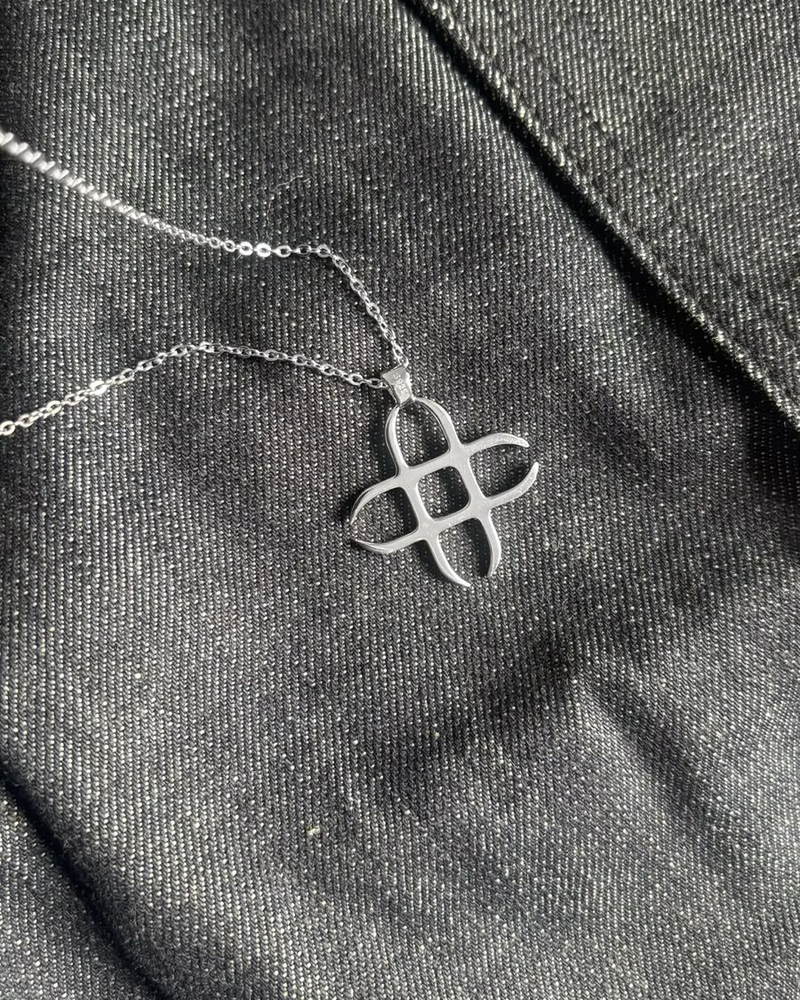 Silver Signature : pendentif croix entrelacée en argent 925 poli sur chaîne, posé sur denim brut